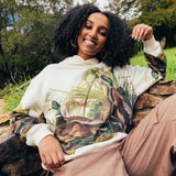 A woman sitting outdoors wearing a cream pullover Oaklandish hoodie with Mallards printed all over. 