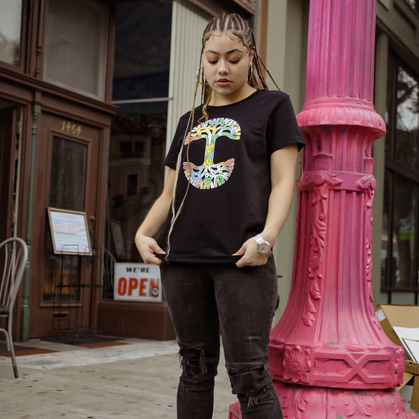 Woman standing outside in Oakland in black t-shirt with full color Oaklandish tree logo, with small tree logo details inside.