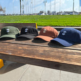 Photo image (left to right) of Olive, Black, Brown and Navy dad hats with embroidered micro Oaklandish logos outside on a bench.