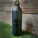 Black aluminum 24 oz waterbottle with black Oaklandish tree logo and wordmark sitting outside on the grass.