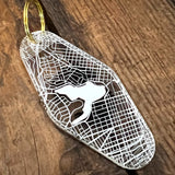 The backside of a translucent plastic motel keychain with an Oakland aerial view map with Lake Merrit on a wood table.