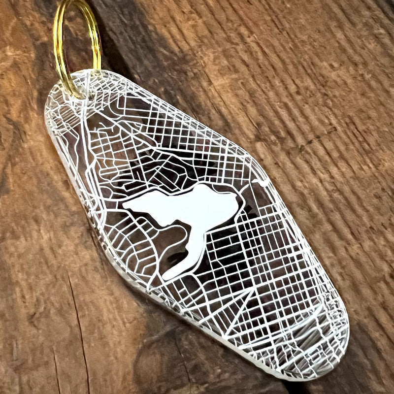 The backside of a translucent plastic motel keychain with an Oakland aerial view map with Lake Merrit on a wood table.