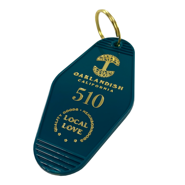 Detailed angle image of blue vintage motel-style keychain with gold Oaklandish Logo and wordmark and 510 local love logo.