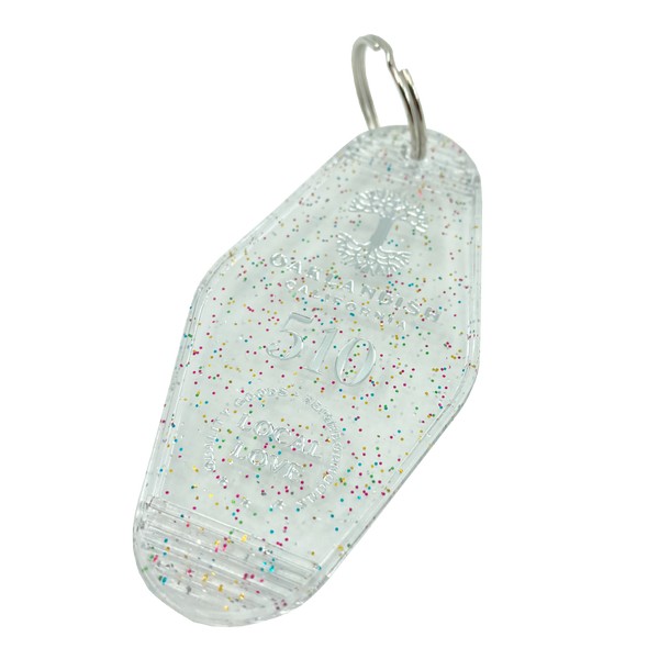 Detailed angle shot of translucent white with rainbow glitter motel-style keychain with Oaklandish Logo and 510 local love.