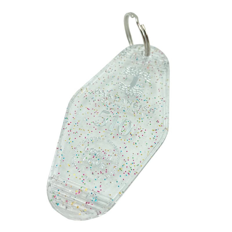 Detailed angle shot of translucent white with rainbow glitter motel-style keychain with Oaklandish Logo and 510 local love.