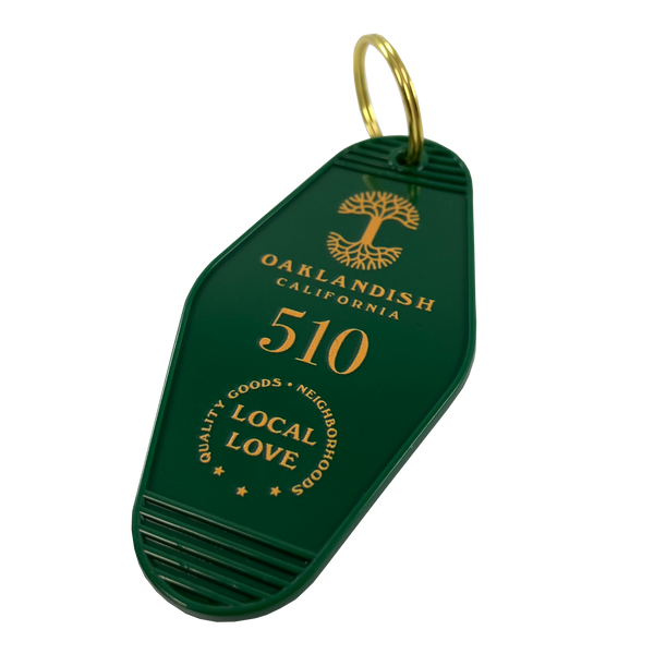 Detailed angle image of green motel-style keychain with gold Oaklandish Logo and wordmark and 510 local love logo.