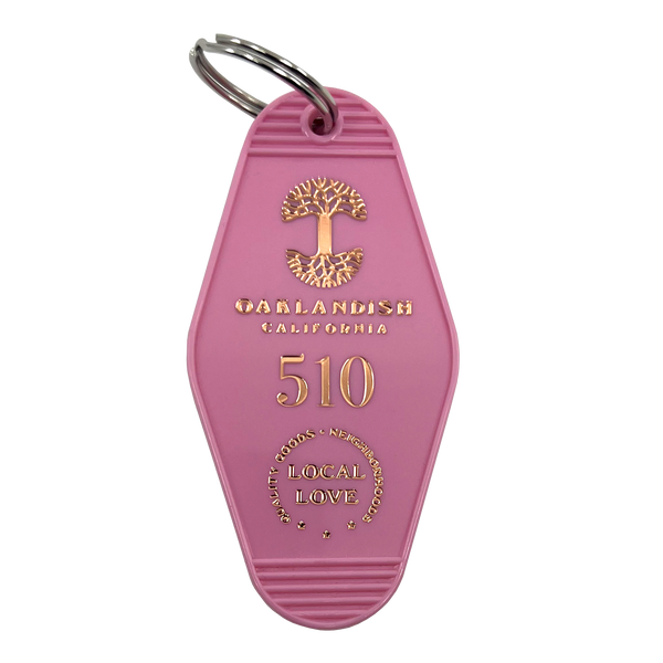 Pink vintage motel-style keychain with gold Oaklandish Logo and wordmark and 510 local love logo.