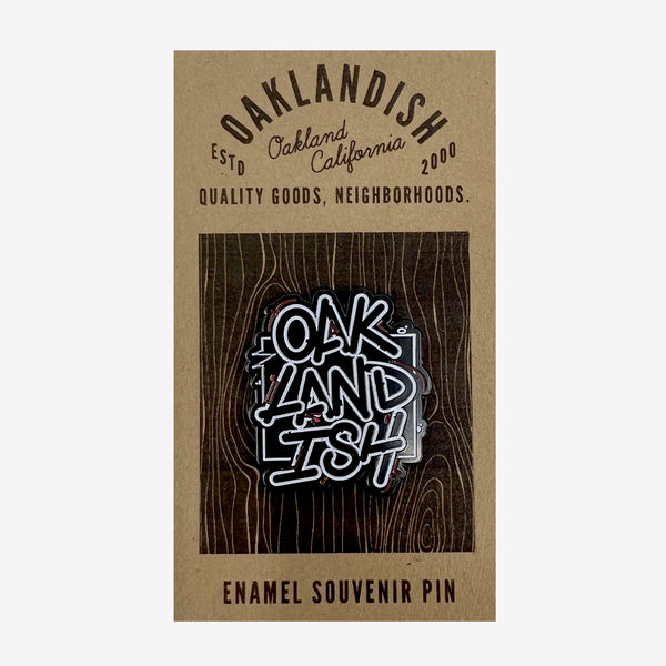 Enamel lapel pin with black and white “Oaklandish” wordmark on brown paper Oaklandish retail packaging.