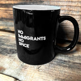 Glossy finish black ceramic coffee mug with white NO IMMIGRANTS NO SPICE wordmark on wood shelf.