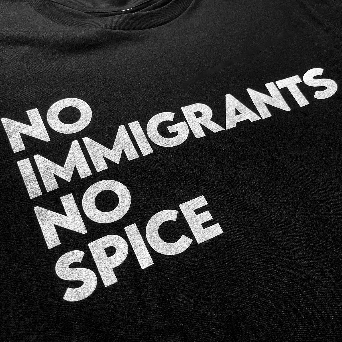 Close-up of white No Immigrants, No Spice wordmark on a black t-shirt.