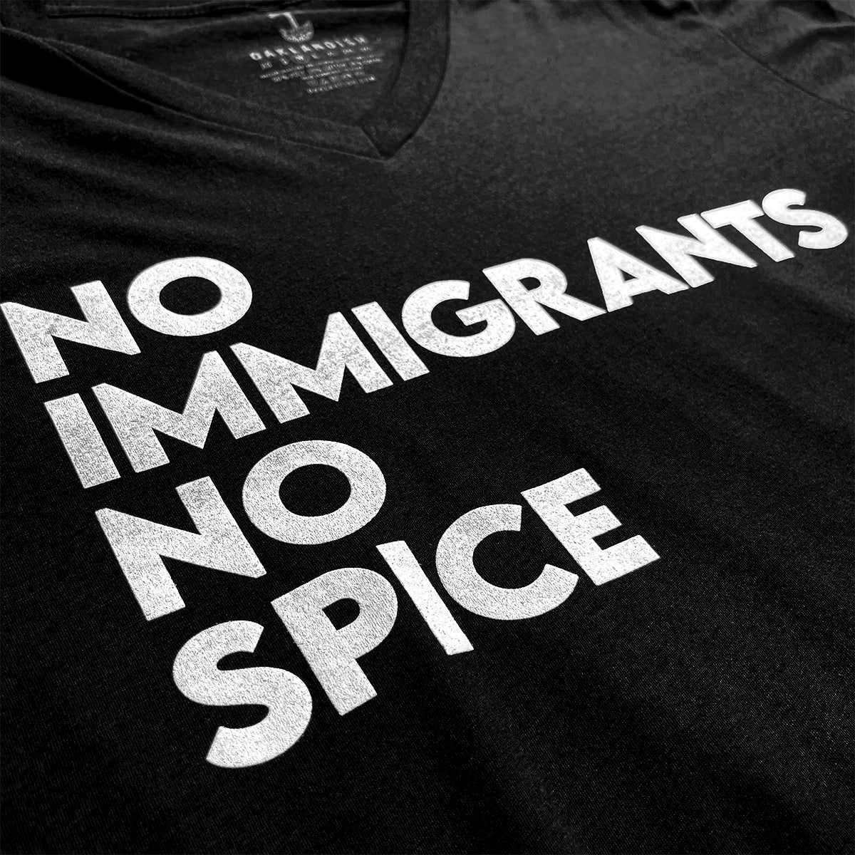 Close-up of white No Immigrants, No Spice wordmark on a black V-neck t-shirt.