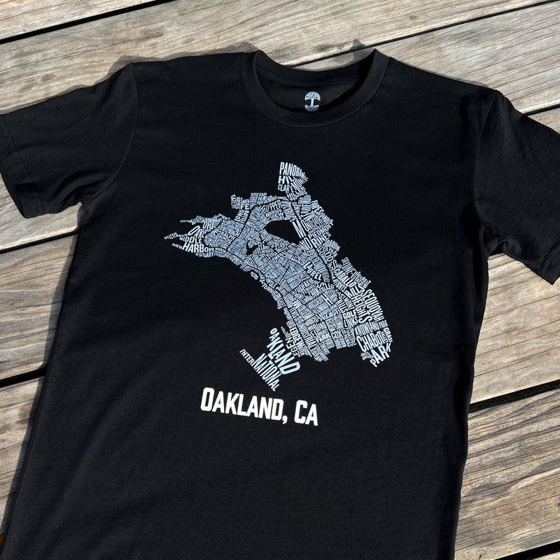 A black t-shirt with an Oakland neighborhood map and the words Oakland CA on a wood deck. 
