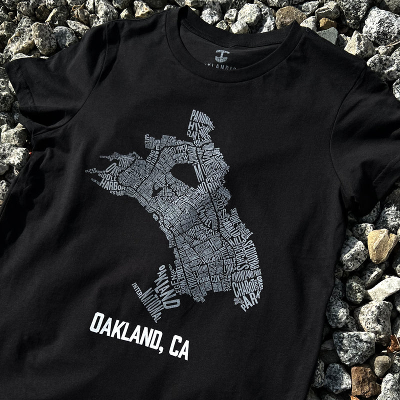 Black t-shirt with an Oakland neighborhood map  & Oakland CA wordmark on rocks.
