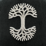 Close-up of silver embroidered Oaklandish tree logo on New Era black corduroy fitted cap.