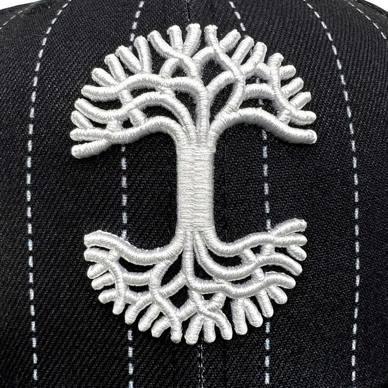 Close-up of white embroidered Oaklandish tree logo on the crown of New Era 59FIFTY black pinstripe fitted cap. 