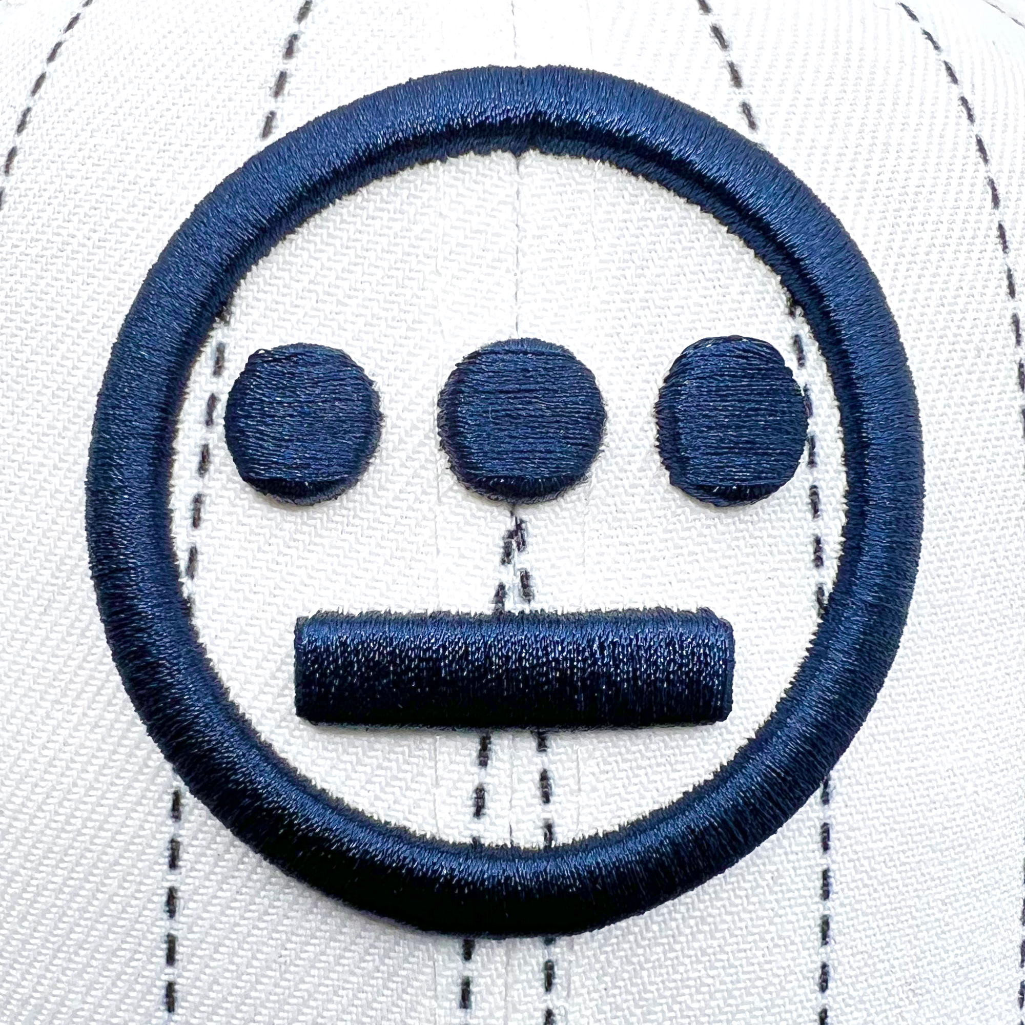 The New Era Hiero Pinstripe 59FIFTY Fitted Cap by Hieroglyphics combines modern style with hieroglyphics-inspired elements. This white cap features black baseball stitching and a black embroidered symbol on the front, with the design showcasing a minimalist face consisting of a circle enclosing three filled circles in a row at the top and a horizontal line at the bottom.