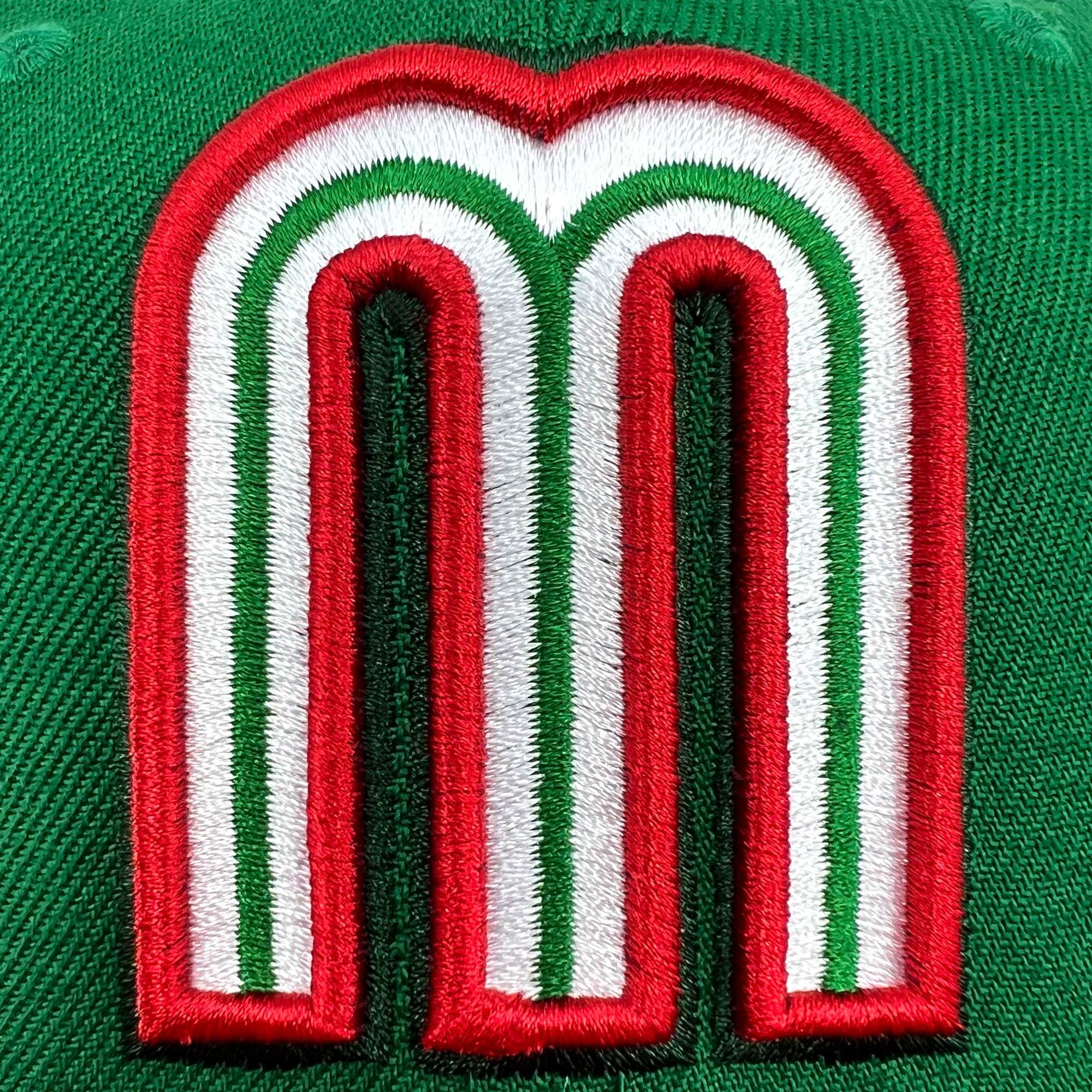 Detailed close-up of red and white Mexican baseball M patch on the crown of New Era cap.