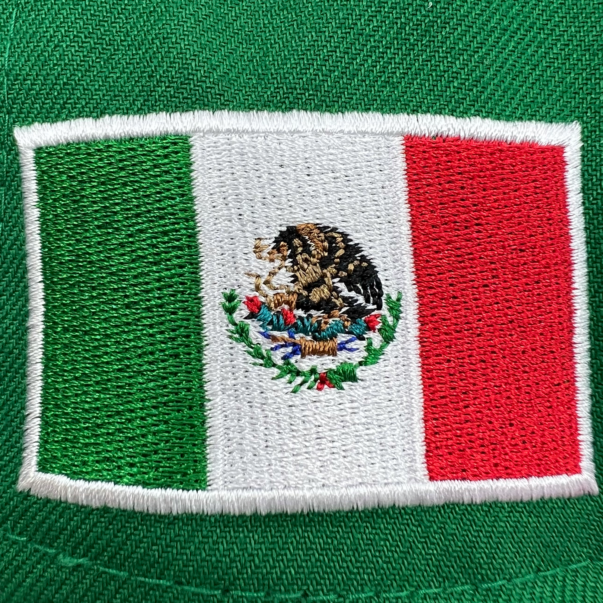 Detailed close-up of the embroidered Mexican flag patch on green fitted New Era cap.