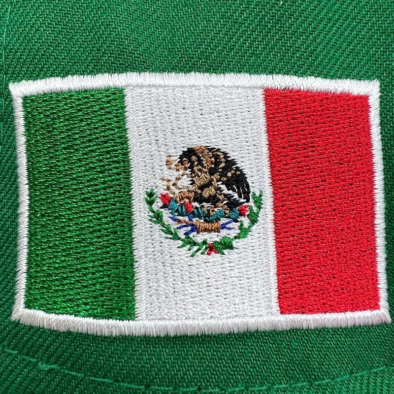 Detailed close-up of the embroidered Mexican flag patch on green New Era cap.