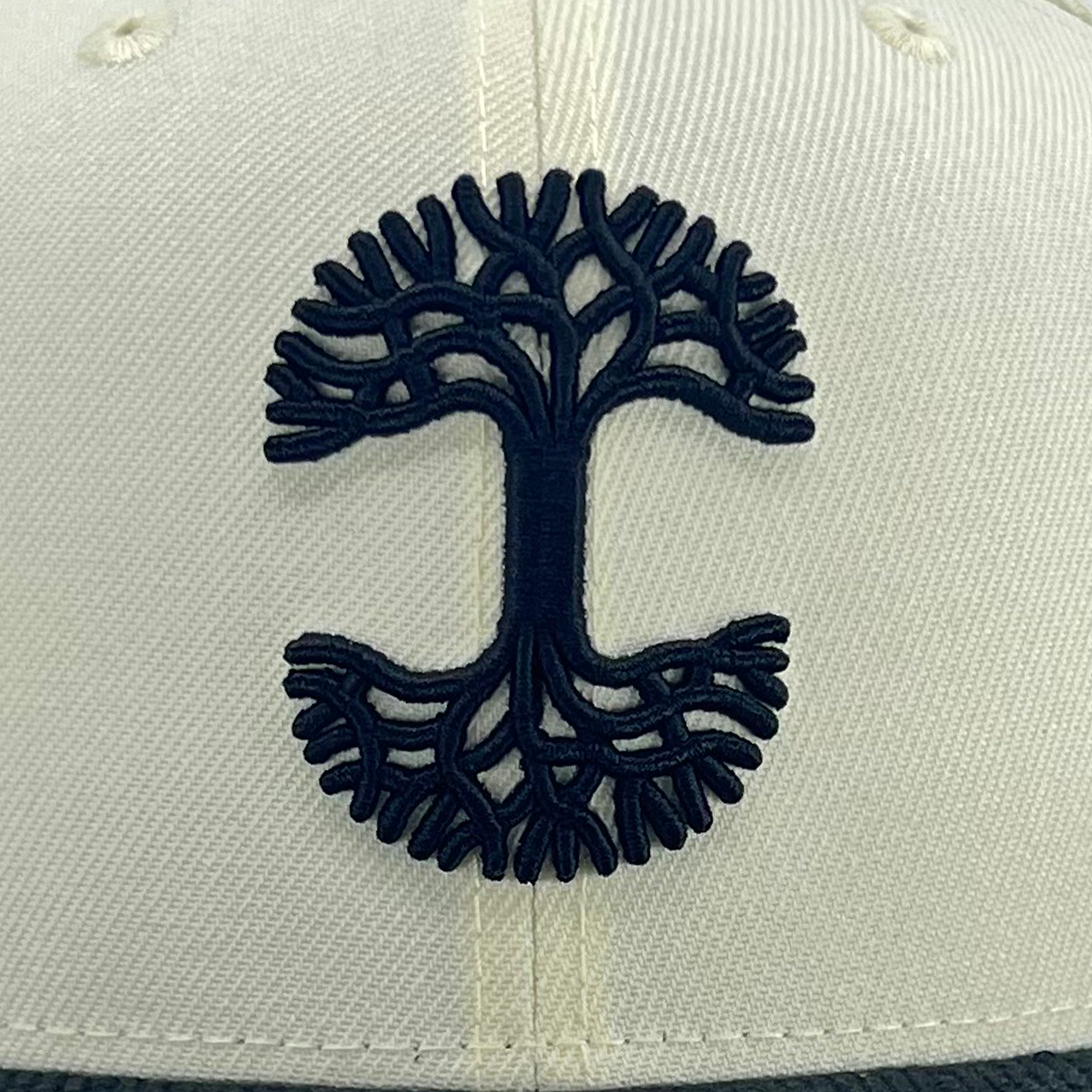 Close-up of black embroidered Oaklandish tree logo on Fitted New Era 59FIFTY cap in chrome white.