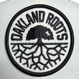 Close up of New Era 59FIFTY chrome fitted hat with a black corduroy brim and black embroidered Oakland Roots SC crest.