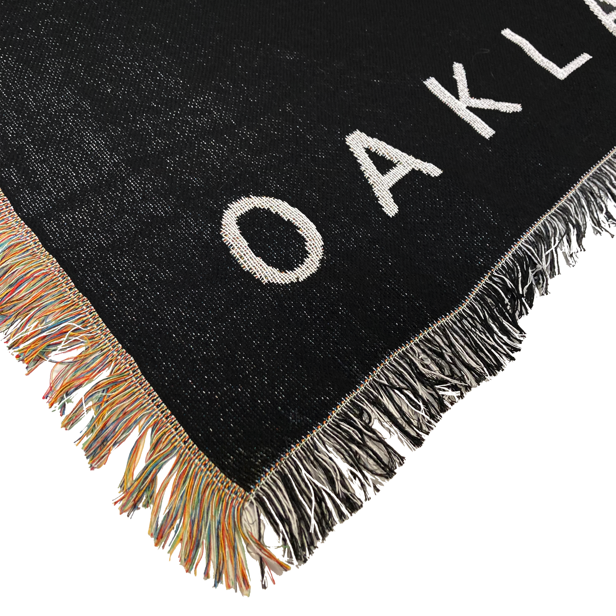 Detailed close-up of the corner of an Oaklandish throw blanket with multi-color fringe on one side and black and white fringe on the other.