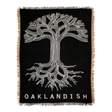 Black throw blanket with large silver Oaklandish tree logo and wordmark with fringe.