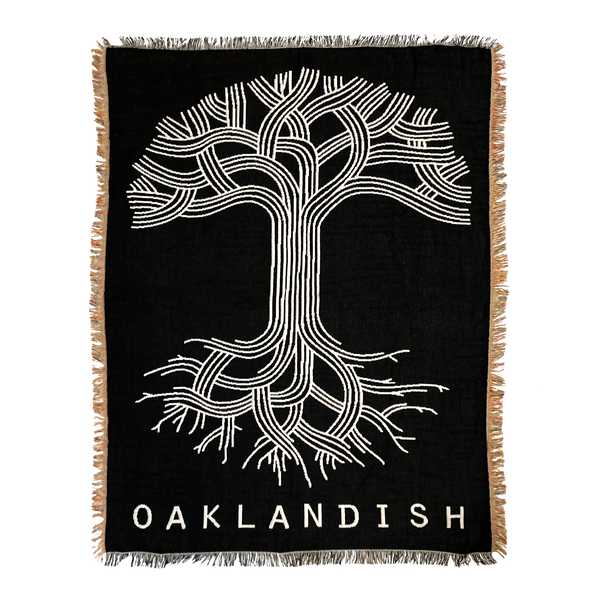 Black throw blanket with large silver Oaklandish tree logo and wordmark with fringe.