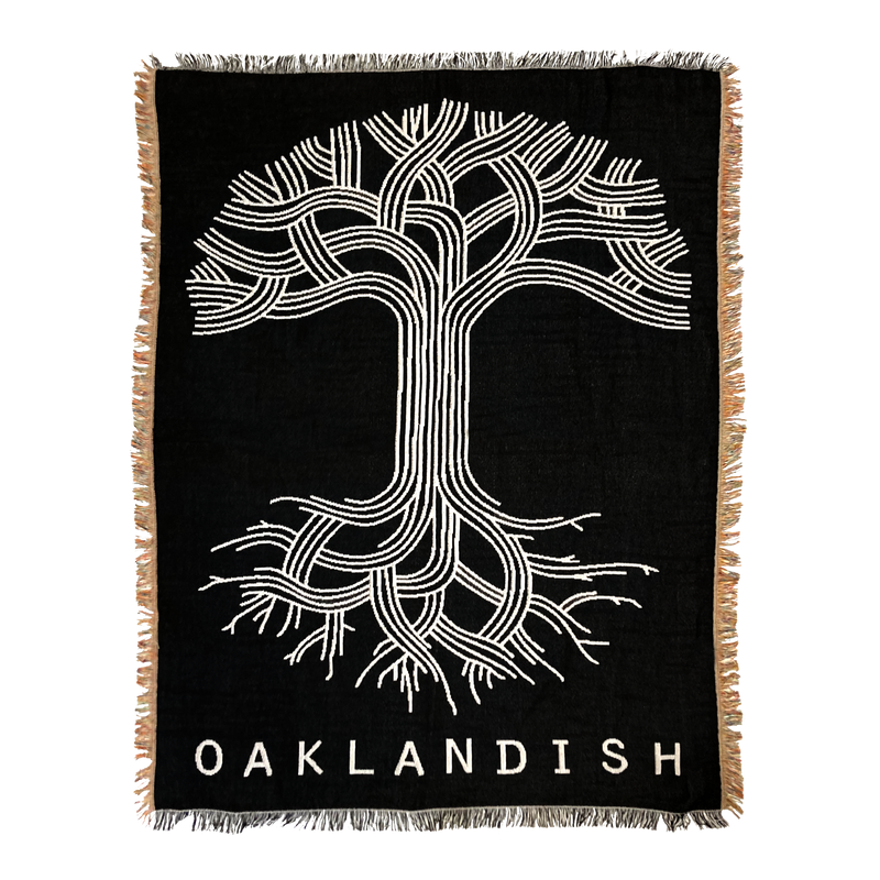 Black throw blanket with large silver Oaklandish tree logo and wordmark with fringe.
