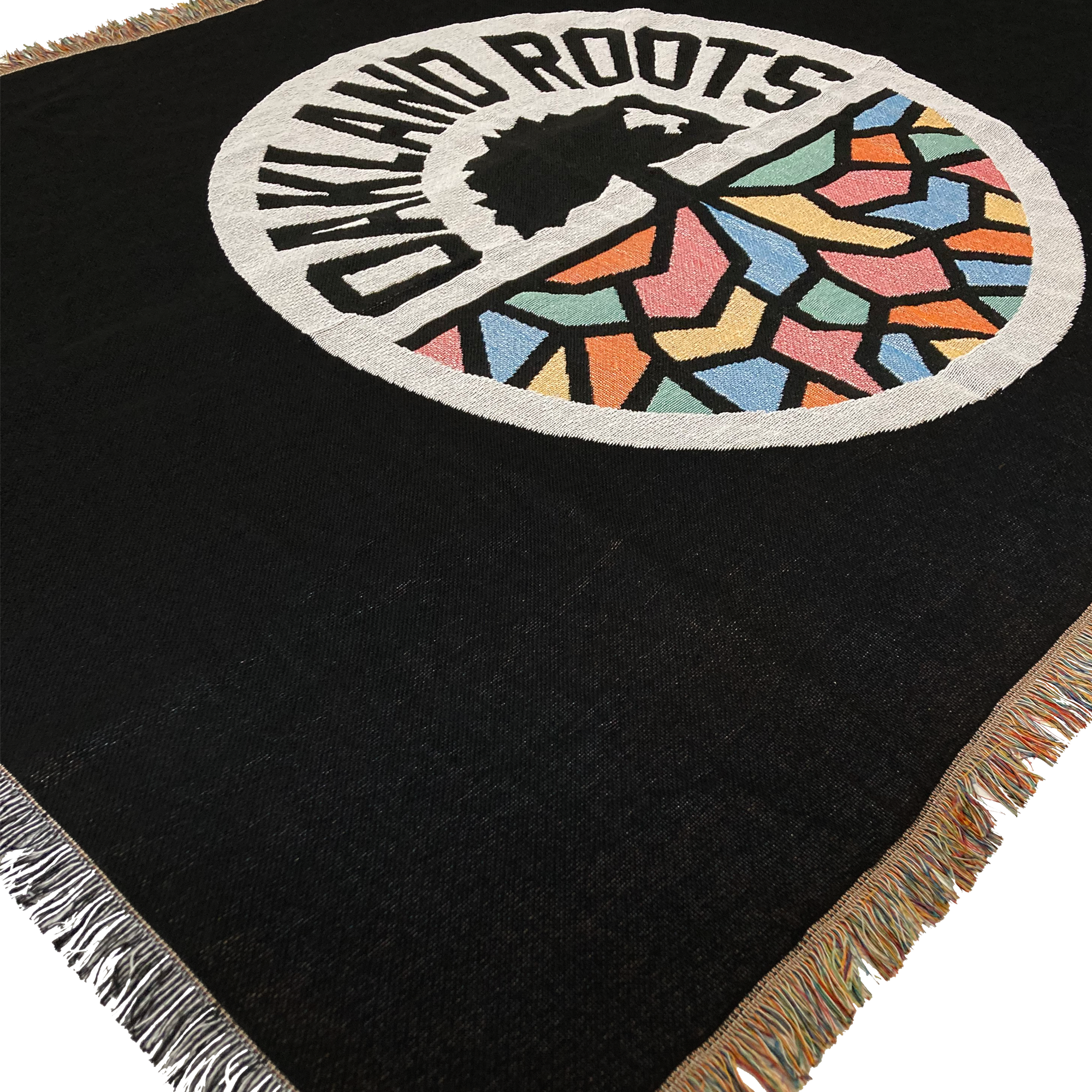 Detailed close-up of a black blanket with colored fringe and large full-color Oakland Roots SC circle logo in the center.