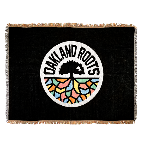 Black blanket with colored fringe and large full-color Oakland Roots SC circle logo in the center.