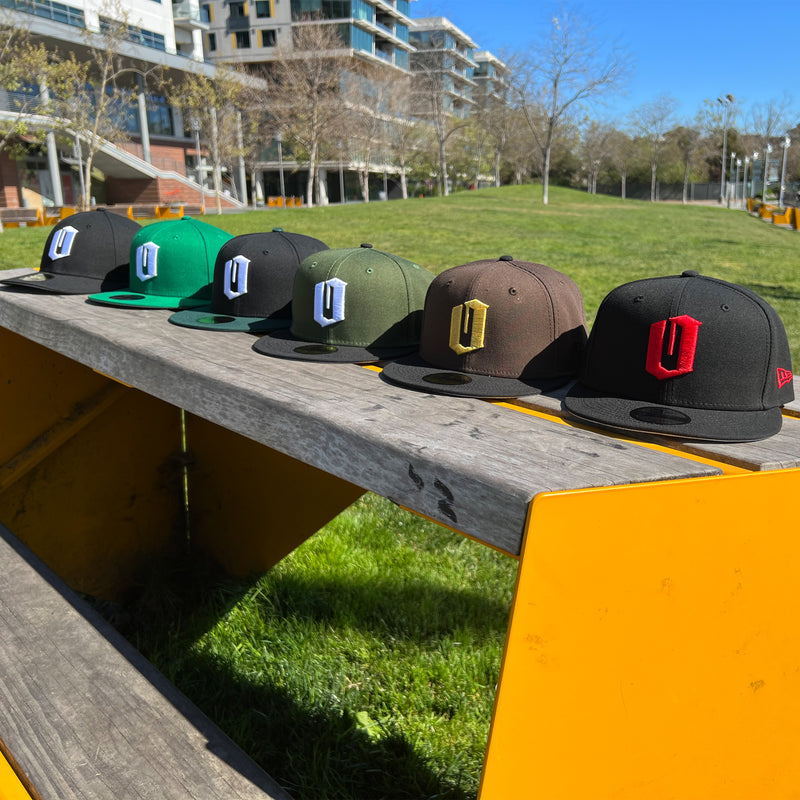 All 6 colorways of New Era Official 9FIFTY Snapback caps with embroidered O for Oakland displayed on an outdoor bench.