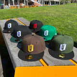 All 6 colorways of New Era Official 9FIFTY Snapback caps with embroidered O for Oakland displayed on an outdoor park bench.