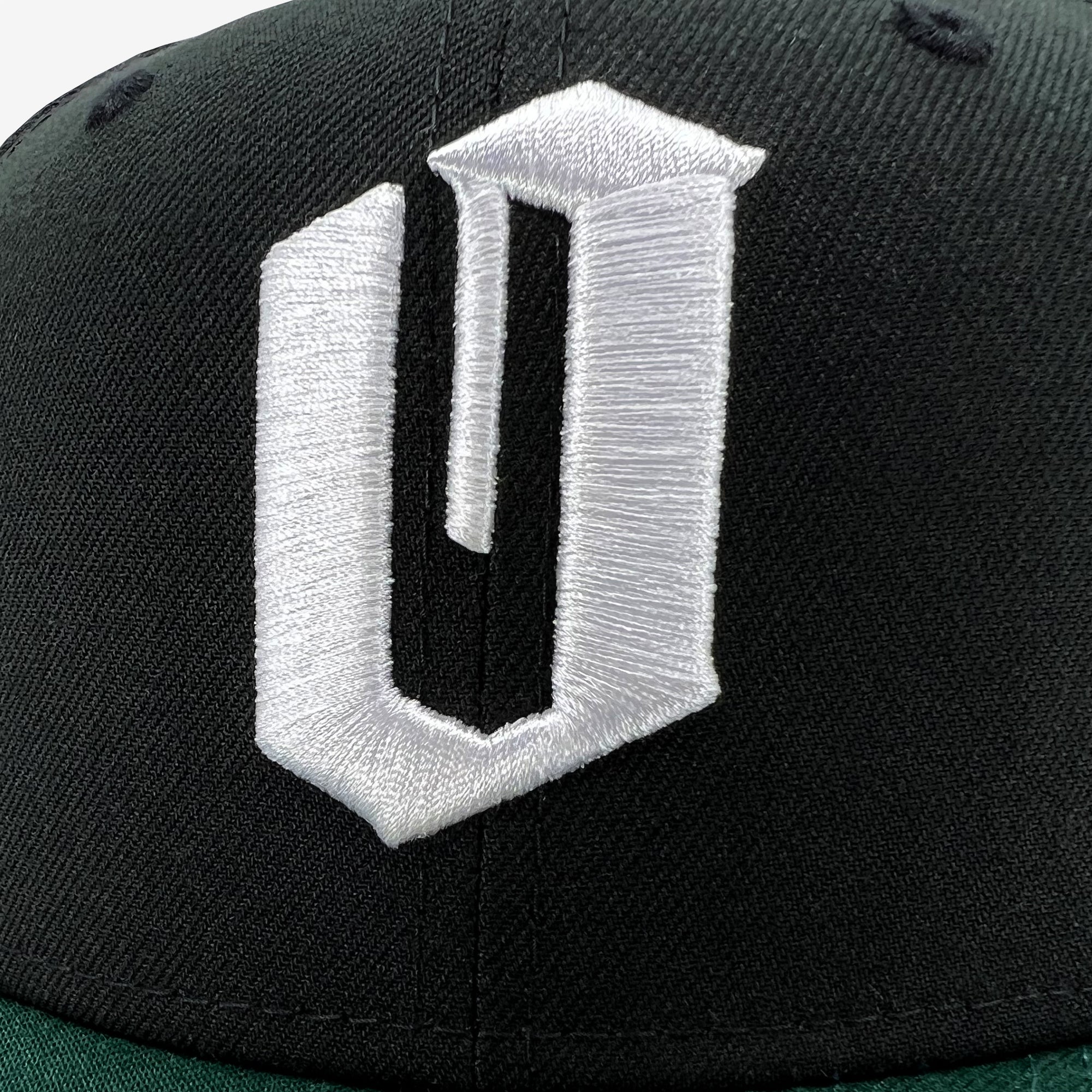 Close up of white embroidered O for Oakland on black New Era cap with green bill.