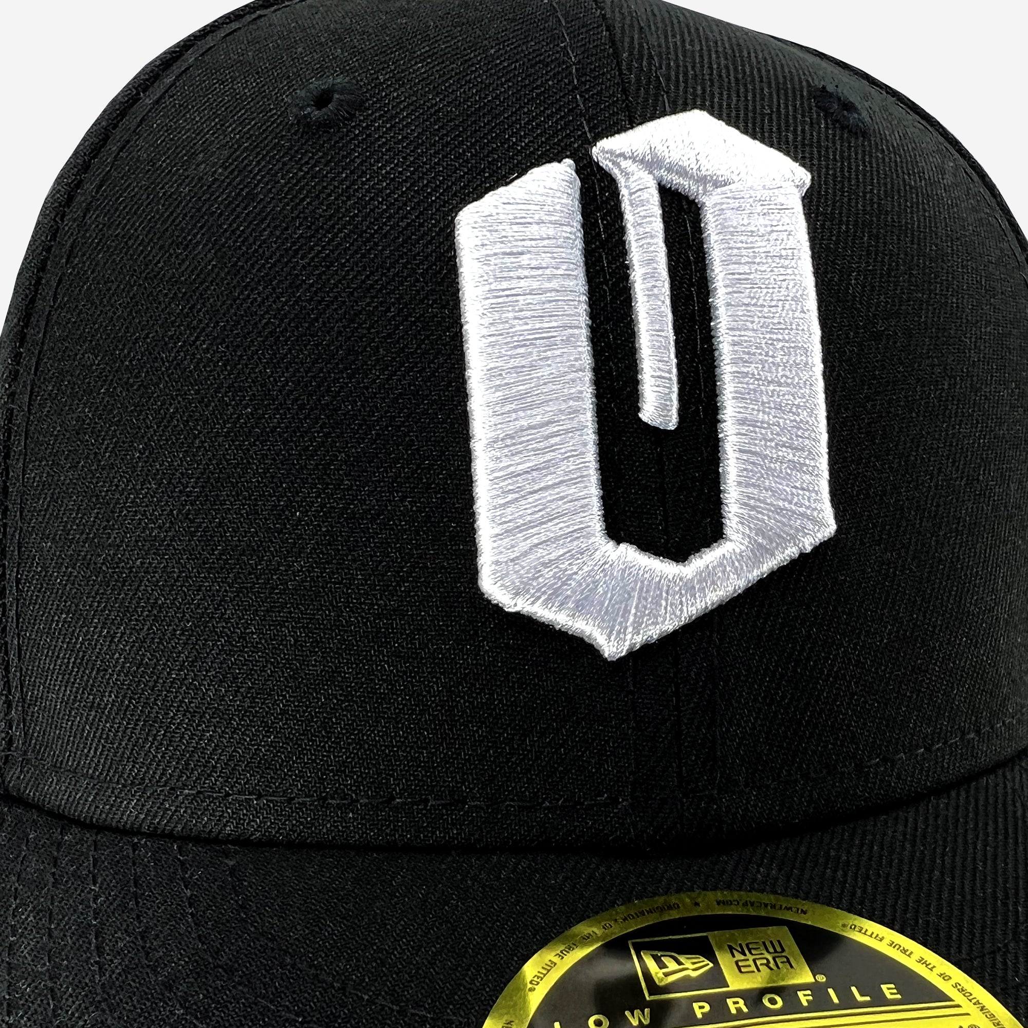 Close-up of embroidered white O logo on a black New Era cap.