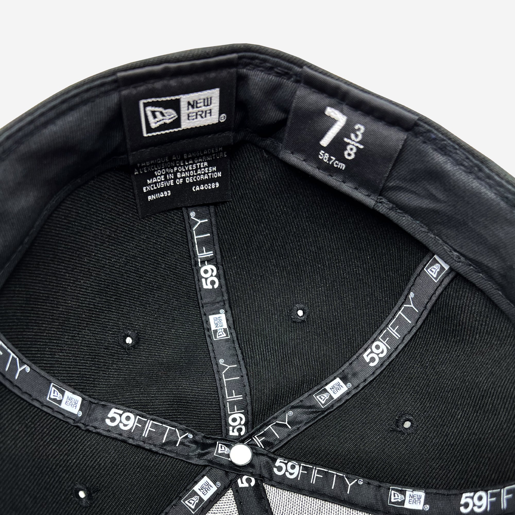 The image displays the interior of a black New Era Official Low Profile 59FIFTY Fitted Cap by Oaklandish. It highlights the size label, indicating it’s 7 3/8 or 58.7 cm. The interior details include branded taping and labels that specify the cap's material composition, manufacturing location, and care instructions from Oaklandish.