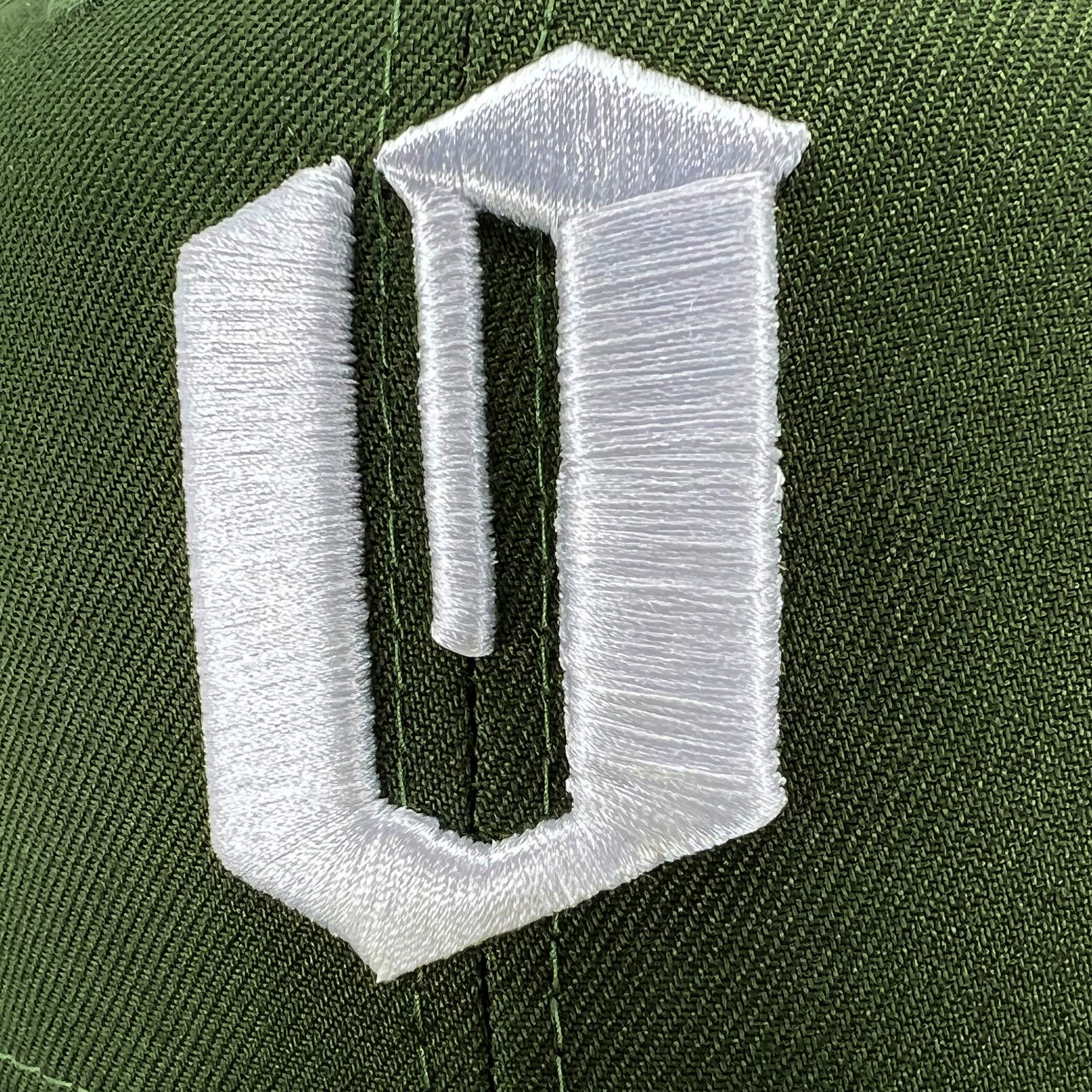 Close-up of an embroidered white O logo on a green cap.