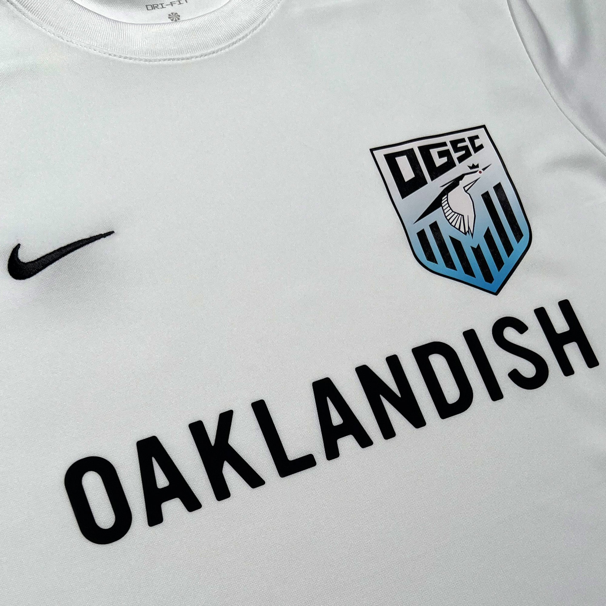 Close-up of Oaklandish wordmark, Oakland Genesis heron logo, and Nike logo on white soccer jersey. 