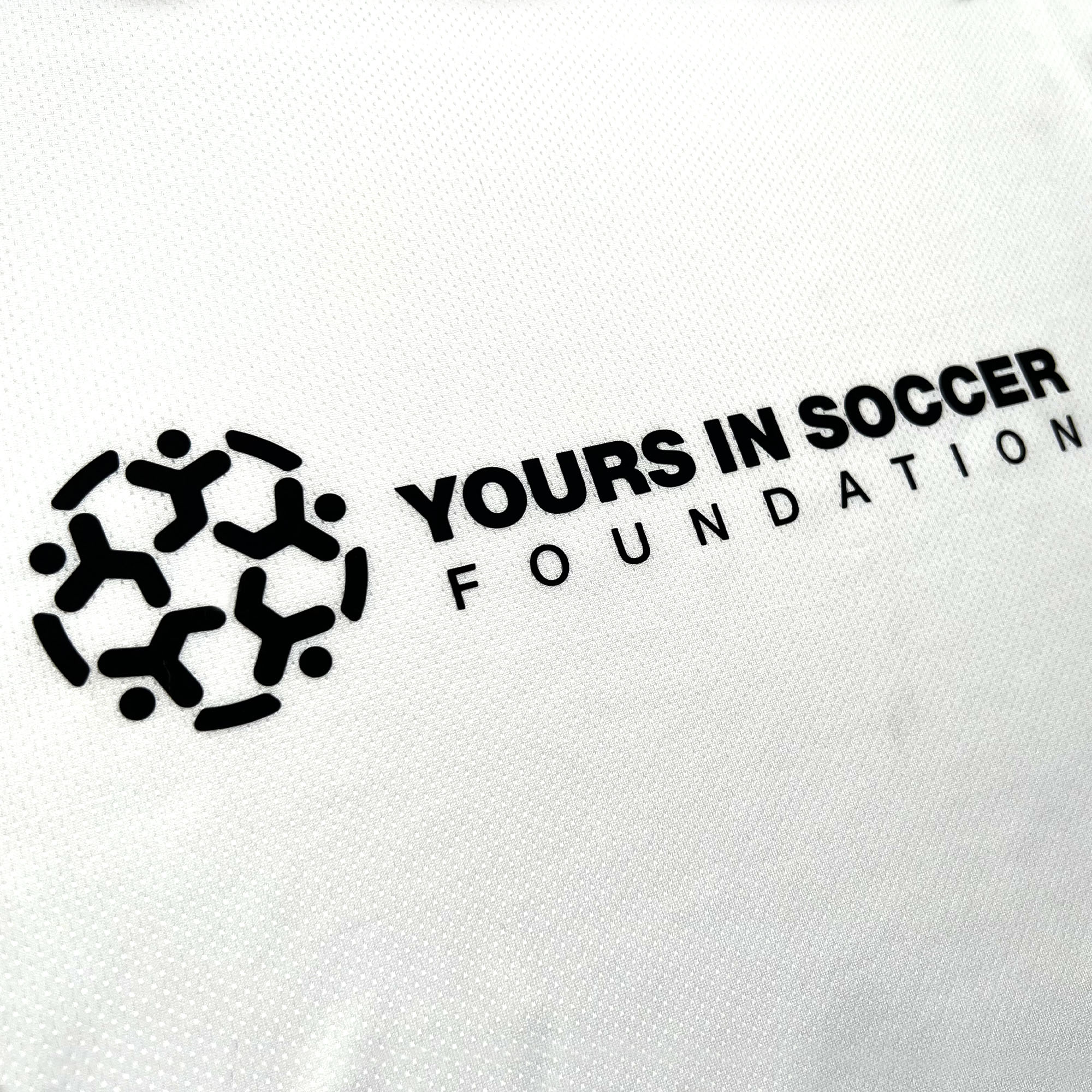 Close-up of Yours in Soccer Foundation logo on white soccer jersey.
