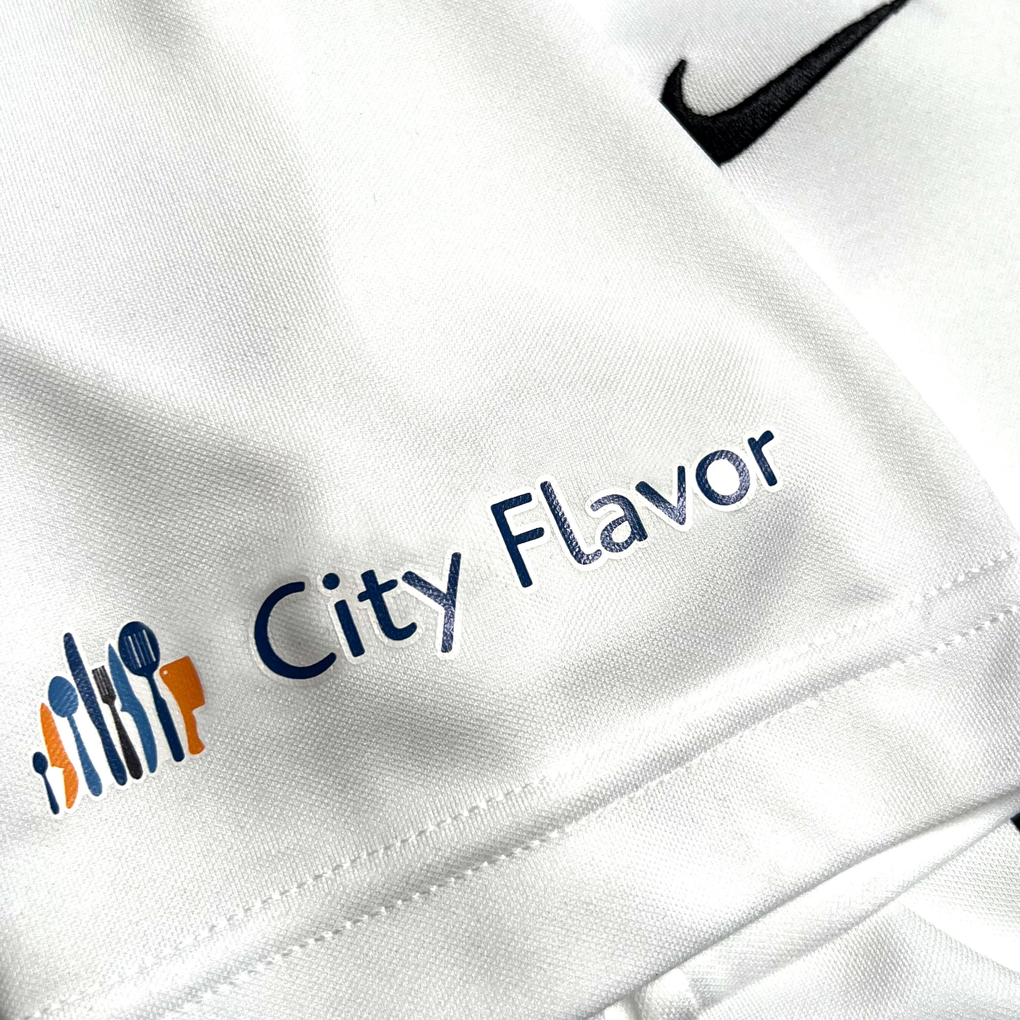 Close-up of City Flavor logo on the sleeve of a white soccer jersey.