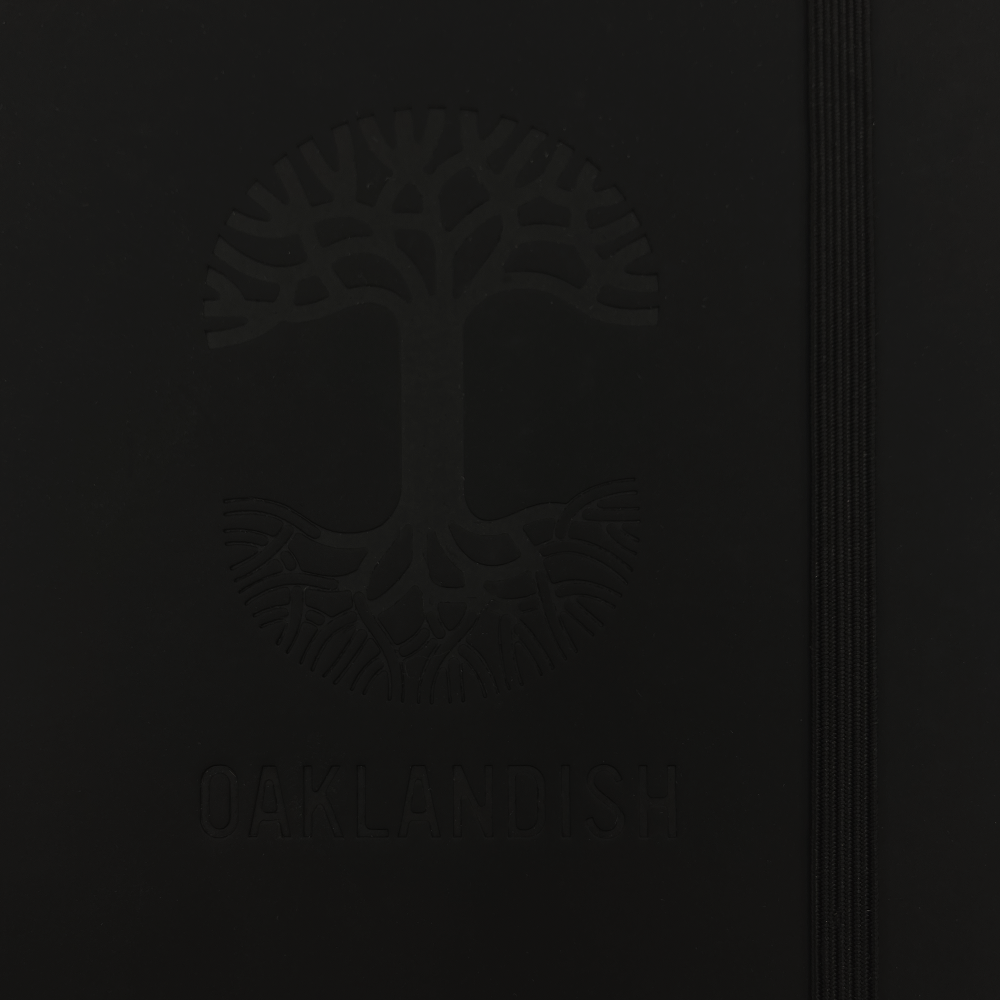 Detailed close-up of Oaklandish tree logo on the front of a black journal notebook.