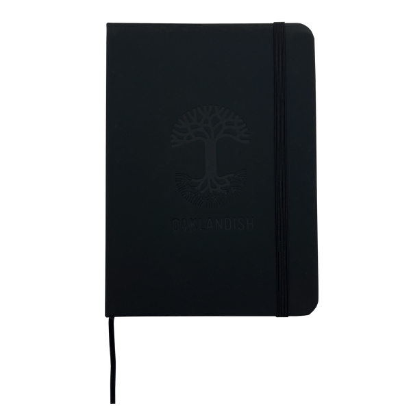 Top view of black Oaklandish journal notebook with elastic closure and bookmark with Oaklandish tree logo and wordmark on the cover. 