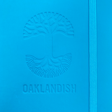 Detailed close-up of embossed Oaklandish tree logo on the front of a blue journal notebook.