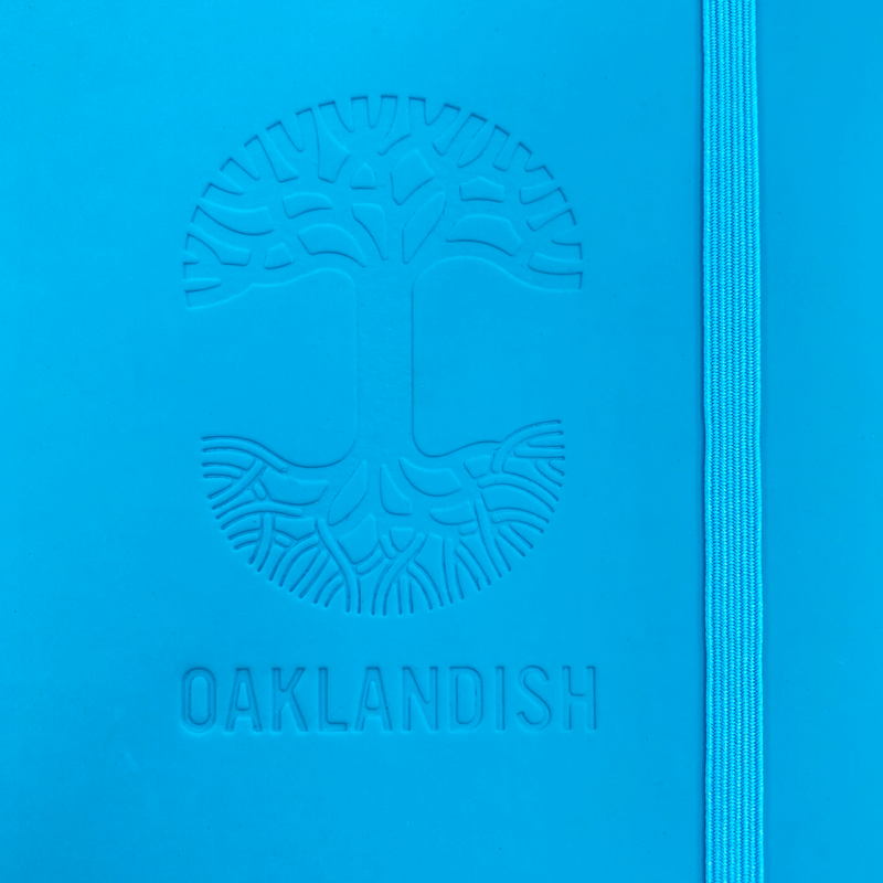 Detailed close-up of embossed Oaklandish tree logo on the front of a blue journal notebook.