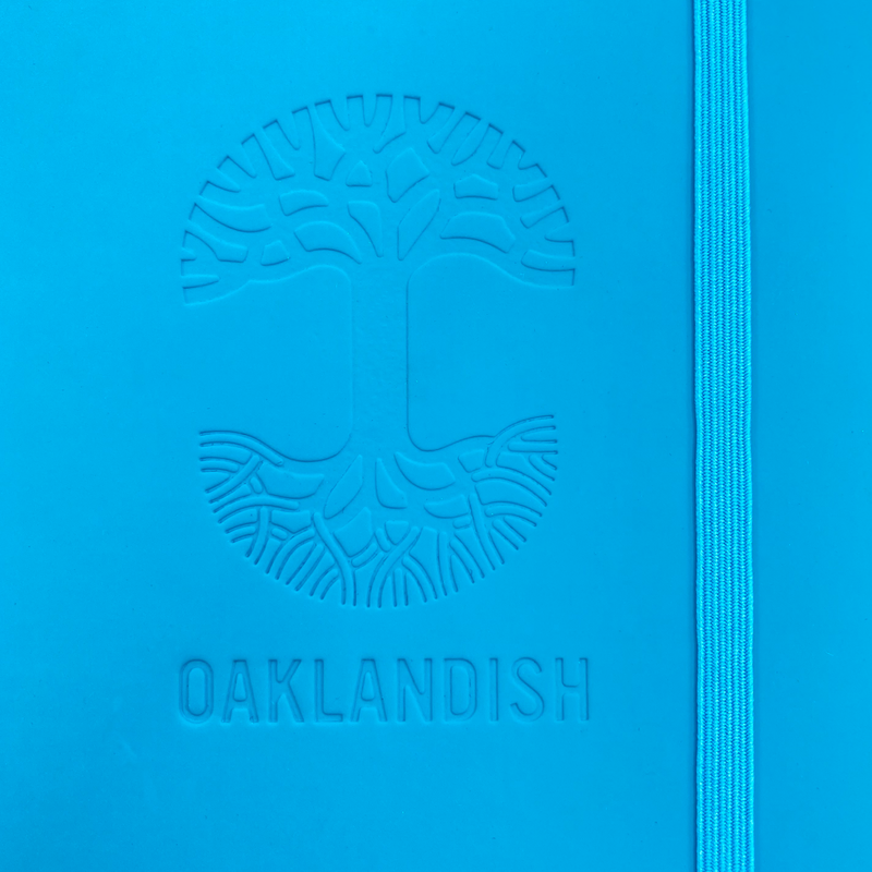 Detailed close-up of embossed Oaklandish tree logo on the front of a blue journal notebook.