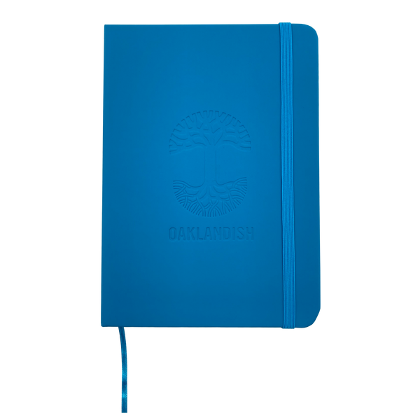 Top view of blue Oaklandish journal notebook elastic closure and bookmark with Oakalndish tree logo and wordmark embossed on the cover. 