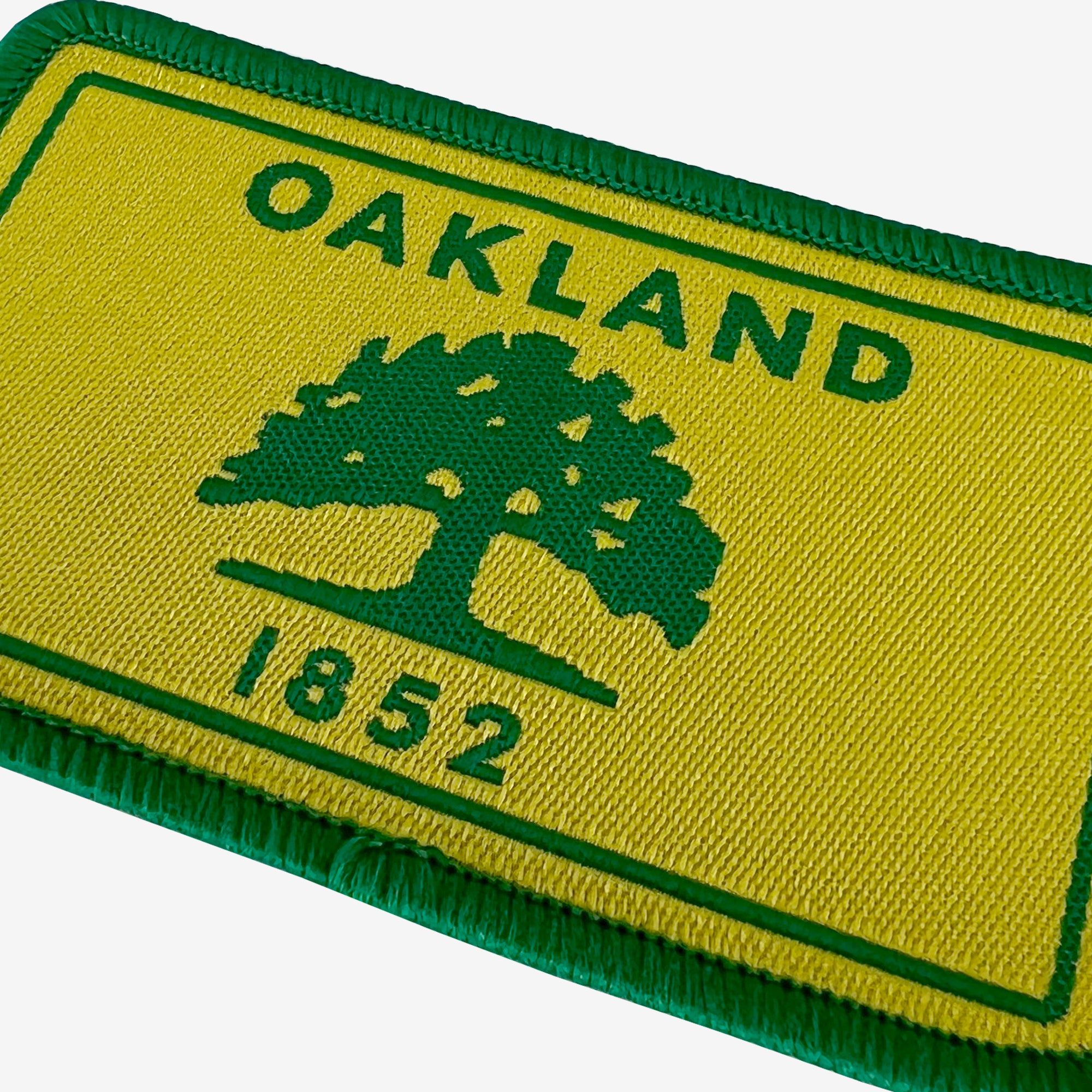 Close-up of gold and green iron-on patch with Oakland 1882 word mark and green tree. 