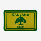 Gold and green iron-on patch with Oakland 1882 word mark and green tree. 