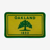 Gold and green iron-on patch with Oakland 1882 word mark and green tree. 