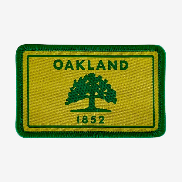 Gold and green iron-on patch with Oakland 1882 word mark and green tree. 